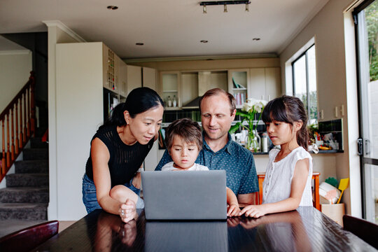 Mixed ethnicity family gathered in front of a laptop on dining table