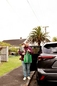 Father carrying toddler son in one arm while other hand carries shopping bag