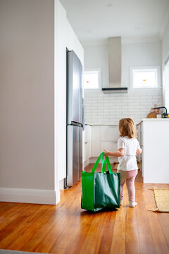 Toddler girl dragging green shopping bag into the kitchen area