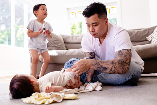 Asian dad changing toddler daughters clothes while lying on carpeted floor