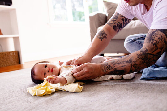 Asian dad changing toddler daughters clothes while lying on carpeted floor