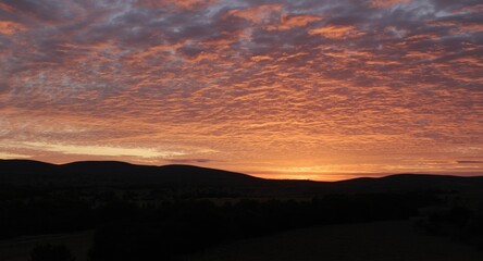 Sunset sky filled with vivid clouds casting warm light on a calm terrain