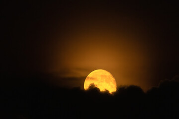 A bright full moon in the night sky partially covered by clouds.