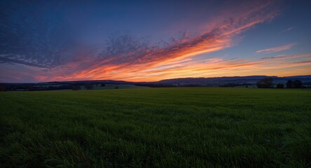 Obraz premium Peaceful twilight scene with a broad lush field, mild rolling hills, and colorful sky