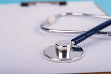 Extreme close-up of a stethoscope on a white clipboard with copy space. Minimalist medical background for healthcare insurance, clinical documentation, and hospital service concept.