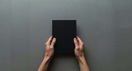 Naklejka premium Copy space included in overhead view of black booklet grasped by mens hands on muted gray surface