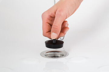 Young adult woman hand fingers holding dark black rubber stopper and opening or closing bathtub drain. Closeup. Front view.