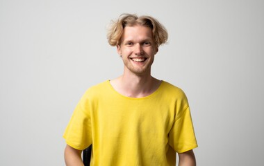 Happy young blonde man smiling confidently, radiating positivity and joy, celebrating success, feeling good, standing relaxed in a comfortable yellow shirt