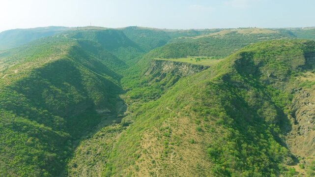 Aerial view of green valleys with steep mountain ridges and a deep canyon during the khareef monsoon in Salalah, Oman.