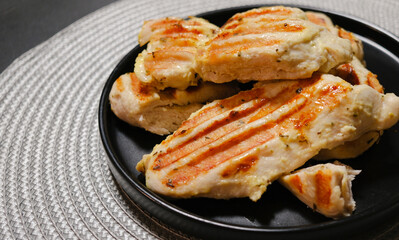 Juicy grilled chicken breast with charred edges on a dark plate. High-quality photos for menu design, healthy eating, and recipe illustrations.