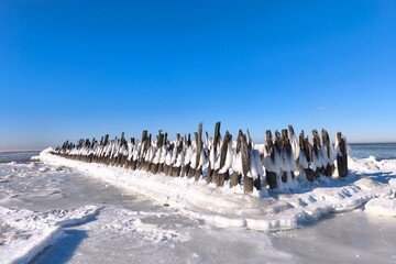 Ice-covered winter pier leading into frozen sea under clear blue sky, minimal cold season background.