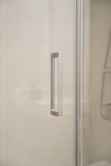 Modern and minimalist shower door handle made of brushed metal on a glass partition, creating a clean, sleek design element in a contemporary bathroom interior