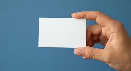 Fototapeta premium Hand holding blank white business card on blue background for corporate branding and professional identity design mockup template.