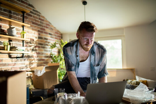 Bearded man running small business from home with laptop and shipping boxes