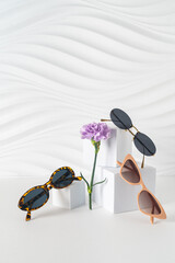 New trendy sunglasses collection on podiums on white background with flowers. Brand new summer...