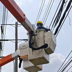 Lineman electrician worker in aerial work platform bucket truck basket repairing and jointing twisted aerial bundled cable for electrical power distribution grid maintenance. © Best Stocker