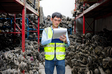 Worker examining auto parts in a warehouse, with stacks of components filling the shelves