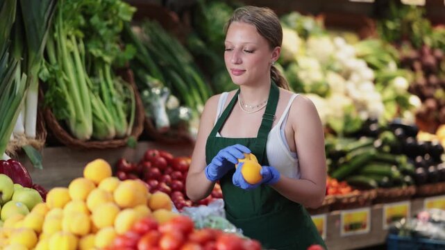 Young saleswoman in a fruit shop carefully lays out yellow peaches on the counter. Supermarket employee monitors the quality of the fruit and checks it before selling it. High quality 4k footage