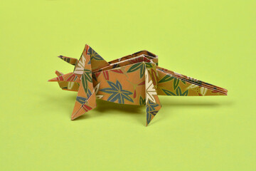 A single handmade paper origami triceratops with a brown and blue floral pattern stands on a solid light green surface © nahhan