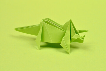 A handmade green paper origami triceratops dinosaur stands on a matching solid green surface in a studio shot © nahhan