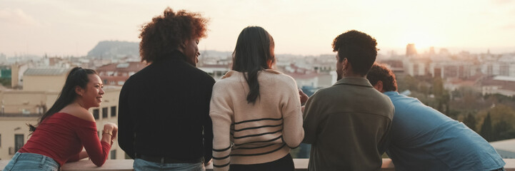 Fototapeta premium Guys and girls at the party, looking at the beautiful views and talking standing on the terrace, friendly party holiday at sunset. Panoramic