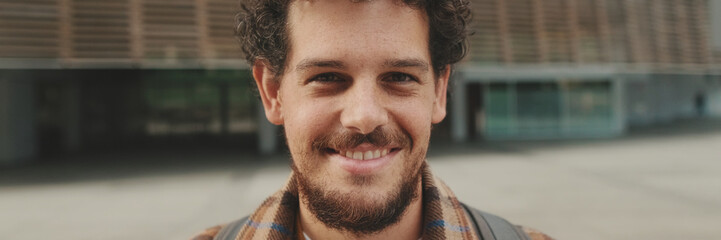 Obraz premium Close up, guy student stands outside the university building looks at the camera and smiles. Panoramic