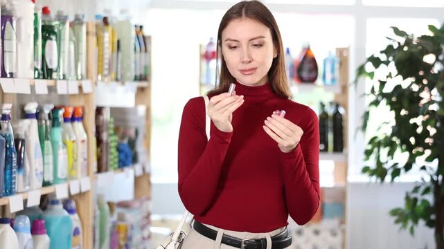 Brunette woman with long hair tries a sample of pink mini lipstick. Customer chooses beautiful shades of lipstick for everyday makeup. High quality 4k footage