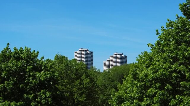 Tall buildings stand above green trees under a clear blue sky in a city setting during daytime