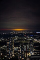 Obraz premium Panoramic Night View of City Skyline with Glowing Orange Horizon and Illuminated Residential High-Rise Apartments