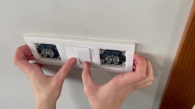 Close-up of hands installing a white decorative frame and plastic buttons on a triple light switch.