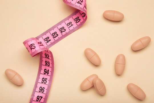 A measuring tape with a variety of colorful pills on beige background. Diet pills, weight loss supplements, and medical dosage control concepts.