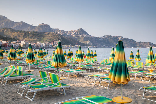 Chairs and umbrellas on an empty beach near the sea in Giardini Naxos