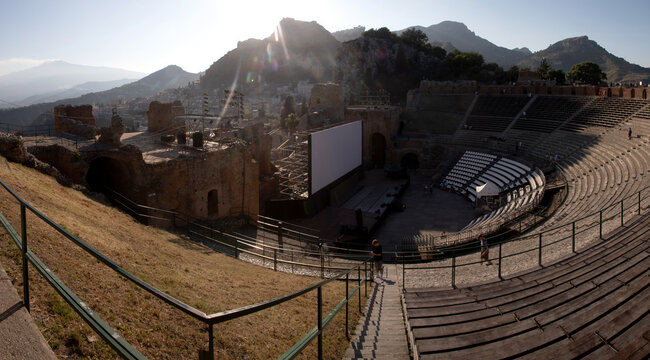 White banner stands in ancient theatre in Taormina surrounded by mountains and ruins, Italy