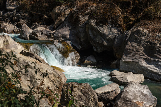 Turquoise mountain river cascading over smooth boulders in Langtang Valley, Nepal, surrounded by rocks and sparse dry vegetation