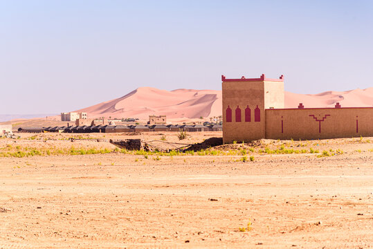 Isolated fortress-like desert building with palm groves and Erg Chebbi dunes beyond in Merzouga