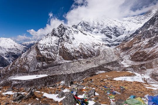 Dramatic view of Langtang Lirung glacier beneath towering Himalayan peaks and prayer flags from Kyanjin Ri, Langtang Valley