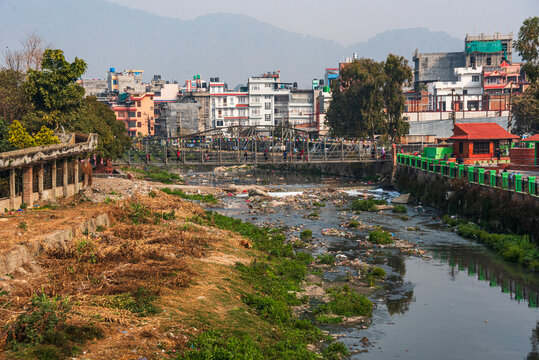 Trash-lined Bishnumati River weaving through dense urban neighborhood in Kathmandu, reflecting challenges of pollution and rapid development
