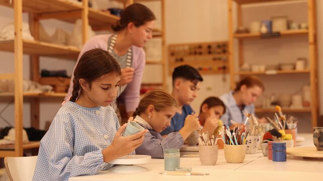 Pleased underage attendees of pottery circle color handmade work-pieces with female instructor