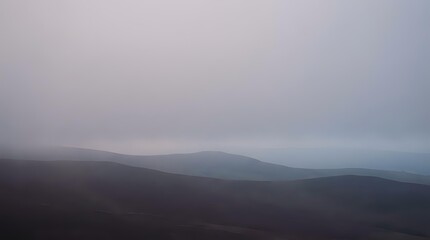 Fototapeta premium Misty mountain landscape with rolling hills shrouded in fog and overcast sky creating moody atmospheric scenery for nature backgrounds and travel content.