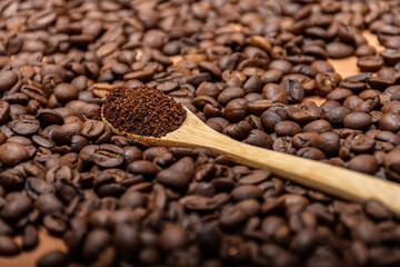 Obraz premium Small wooden spoon with ground coffee on roasted coffee beans.