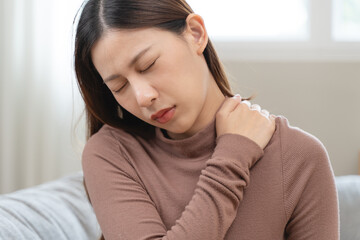 Fototapeta premium muscles stiff problem, suffer young woman, girl face painful, hand holding neck ache from work hand holding massaging rubbing shoulder hurt, sore sitting on couch at home