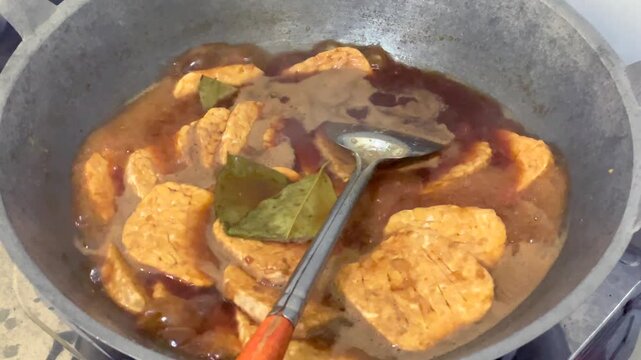 Cooking traditional indonesian sweet marinated tempeh or tempe bacem in a wok