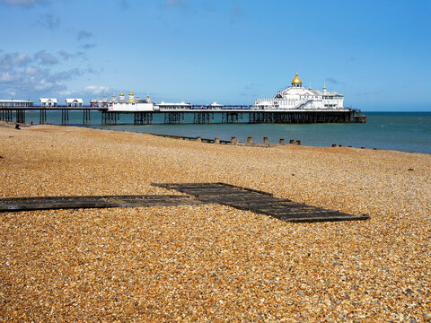Shingle beach with pier in Eastbourne, people walking and enjoying the seaside view in East Sussex