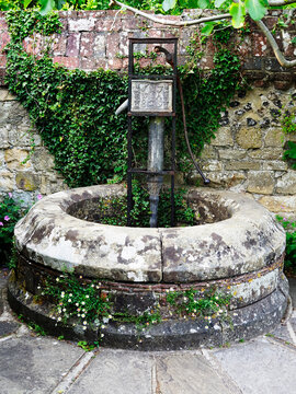 Old water pump surrounded by stone and plants in a garden in Lewes, East Sussex
