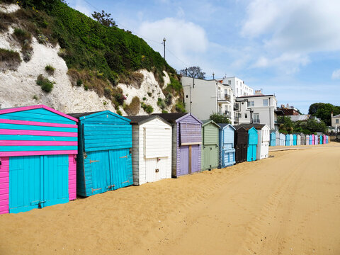 Colorful beach huts lined along the sandy shore in Broadstairs, Kent during sunny weather