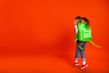 Naklejka premium Young girl with bright green backpack walking against bold orange background showcasing school fashion joy and family friendly vibes
