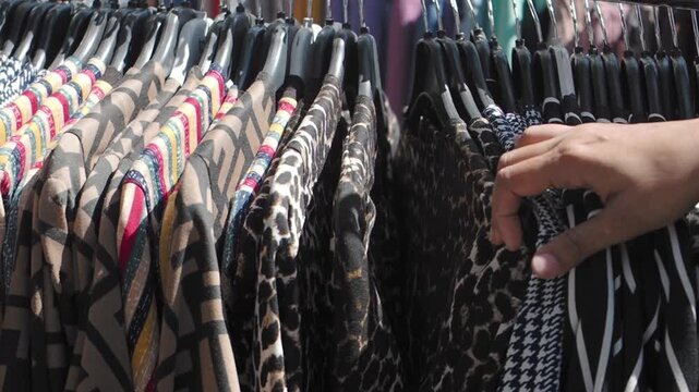 Woman hand browsing through leopard print and patterned clothing on hangers at street market