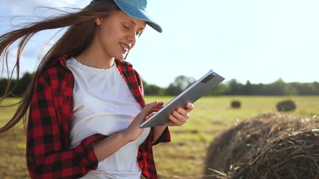 Woman in field holding tablet computer. Girl works on tablet in field. Woman works in a field with haystacks of grass. Lifestyle a woman in a field is holding a tablet.