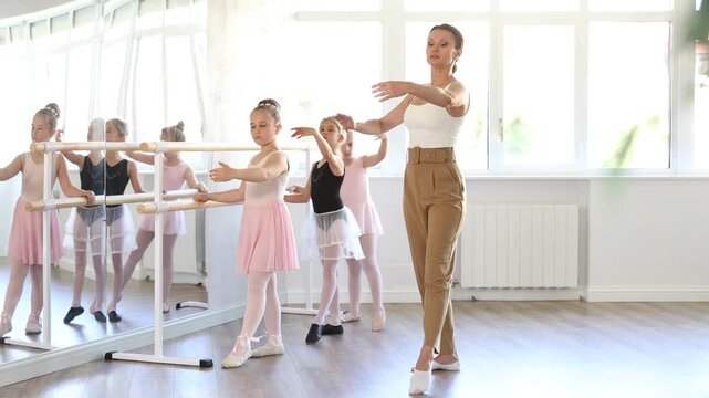During lesson in choreography class, girls repeat movements of teacher and perform Batman element. Aesthetic types of dance sports for children under guidance of coach