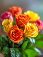Fototapeta premium Vibrant bouquet featuring a mix of yellow, orange, pink, and red roses with lush green leaves creating a bright and cheerful floral arrangement